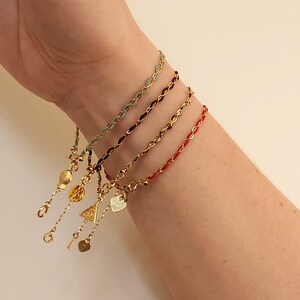 Peut inclure: Quatre bracelets délicats en vert, bordeaux, or et rouge sont présentés. Chaque bracelet présente un motif de chaîne tissée avec des accents dorés. Des breloques, dont un poisson, un triangle, une clé et un cœur, ajoutent des détails.