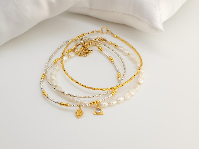 May include: Set of four delicate gold and silver beaded bracelets with pearl accents and two small charms. The charms are a diamond shape and a triangle with a clear stone in the center.