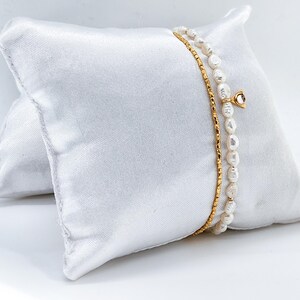 May include: Two gold chain bracelets with white pearl accents. One bracelet has a small gold charm with a clear stone.