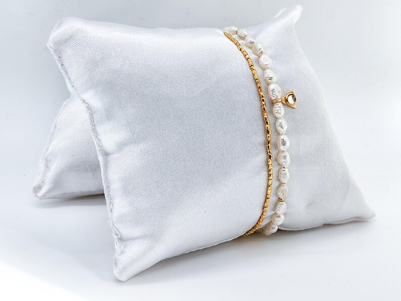 May include: Two gold chain bracelets with white pearl accents. One bracelet has a small gold charm with a clear stone.