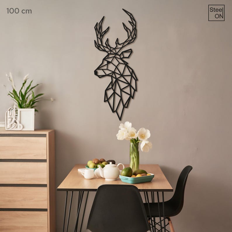 May include: Black geometric deer head wall decor, 100 cm wide, mounted on a light gray wall above a wooden table with two black chairs. The table is set with a teapot, cups, and fruit in bowls.