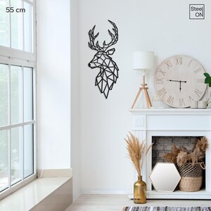 May include: Black metal wall art of a geometric deer head silhouette. The deer head is 55 cm tall and is mounted on a white wall. The deer head is in a living room setting with a fireplace and a clock.