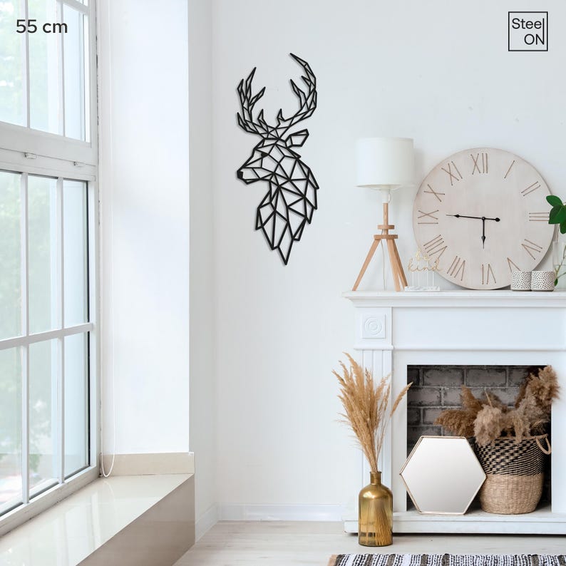 May include: Black metal wall art of a geometric deer head silhouette. The deer head is 55 cm tall and is mounted on a white wall. The deer head is in a living room setting with a fireplace and a clock.