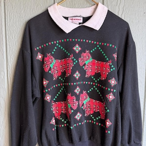 May include: Black sweatshirt featuring a white collar and red tartan dog designs. The sweatshirt has green and red accents, with the brand name "Karen Blake" visible on the collar.