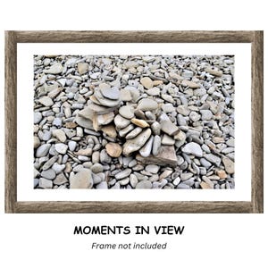 May include: A framed print featuring a collection of smooth, gray and tan stones. A small stack of stones is in the center. The words "MOMENTS IN VIEW" are printed at the bottom, with "Frame not included" below.