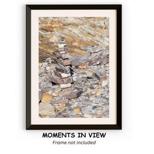 May include: A close-up of a rock formation with a stack of stones in the center. The rocks are a mix of brown, gray, and white. The background is a blurred image of more rocks.