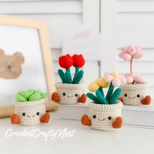 May include: Four crocheted potted plants with smiling faces. The plants are a succulent, a daisy, a tulip, and a pink flower. The pots are all white with brown arms.