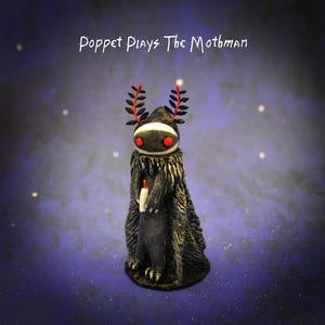 May include: A handcrafted figurine of a creature with a black hooded cloak, red eyes, and a white band across its face. The figure holds a candle and has decorative red and black antlers. The text "Poppet Plays The Mothman" is above the figure.