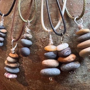 May include: Five necklaces with stacked stone pendants. Each pendant is made of different colored stones and is wired together with silver wire. The necklaces are on a variety of cords, including brown, black, and white.