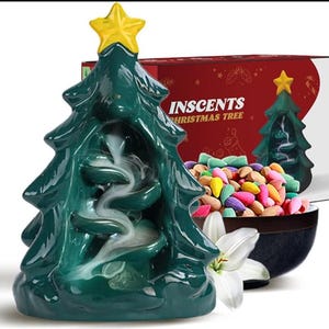 Op de afbeelding: Een groene keramische kerstboom wierookbrander met een gele ster. De brander heeft een wervelend rookeffect. Een doos met de tekst "INSCENTS CHRISTMAS TREE" staat op de achtergrond, samen met een kom met kleurrijke wierookkegels.