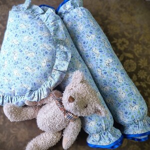 May include: Two blue and white patterned pillow covers with ruffled edges and a teddy bear toy. The pillow covers have a blue trim and are made of soft fabric.