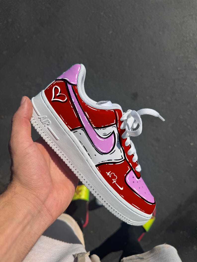 May include: Red and pink Air Force 1 sneakers with a white sole. The sneakers feature a heart design and a pink Nike swoosh. The laces are white.