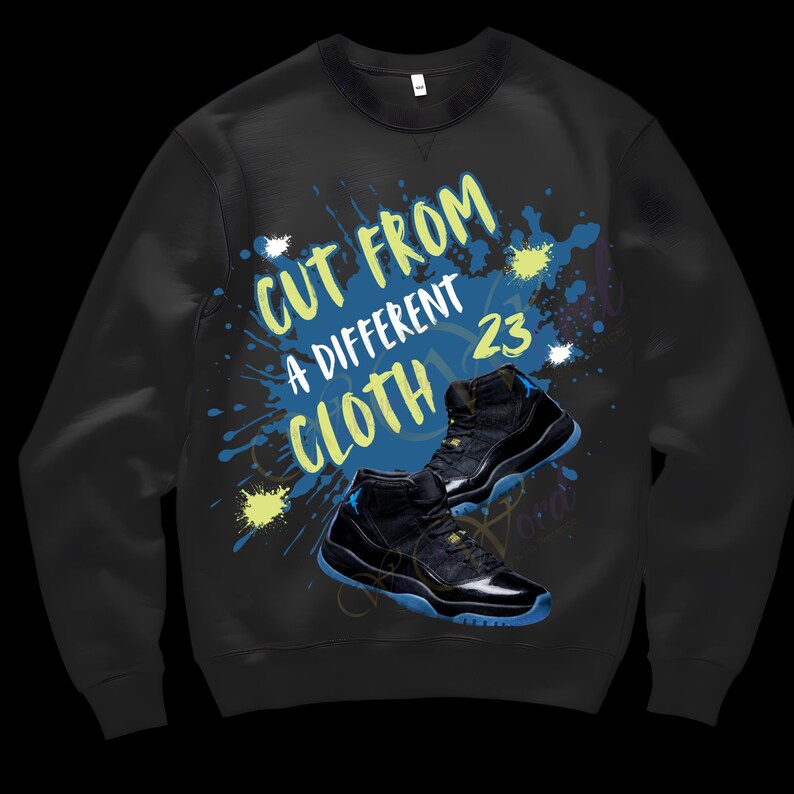 May include: Black sweatshirt with the text "CUT FROM A DIFFERENT CLOTH 23" in yellow and white. The design includes blue and yellow paint splatters and a pair of black and blue sneakers.