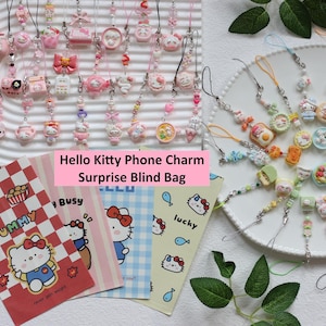 May include: A collection of Hello Kitty phone charms and surprise blind bags. The charms are in various pink and pastel colors, featuring Hello Kitty and related designs. The image includes several small cards with Hello Kitty graphics.