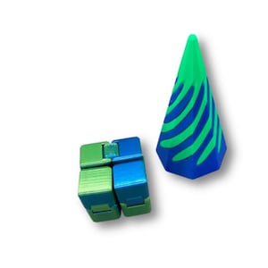 Può includere: Due giocattoli fidget su sfondo bianco. Uno è un giocattolo fidget a forma di cubo con sezioni verdi e blu. L'altro è un giocattolo fidget a forma di cono con strisce verdi e blu. Entrambi i giocattoli sono in plastica.