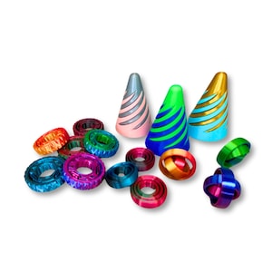 Pode incluir: Uma coleção de brinquedos fidget coloridos, incluindo piões em forma de cone com desenhos listrados em rosa, verde e dourado, e vários spinners em forma de anel em tons de azul, vermelho e roxo. Os brinquedos estão dispostos sobre um fundo branco.