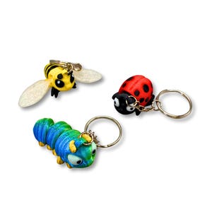 May include: Three novelty keyrings: a yellow and black bee with white wings, a red ladybird with black spots, and a blue and green caterpillar. Each keyring has a silver-coloured ring.