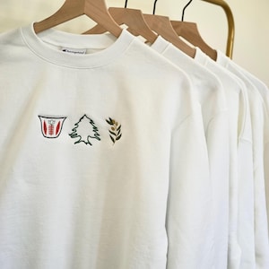 May include: White Champion brand sweatshirt with embroidered green cedar tree, olive branch, and red and white symbol.