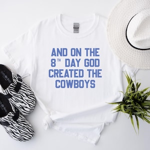 May include: White t-shirt with blue text that reads "And on the 8th day God created the Cowboys".