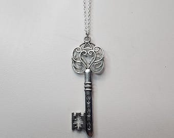 May include: A silver key necklace with a detailed, ornate design. The key has a heart-shaped top and a long, slender shaft.
