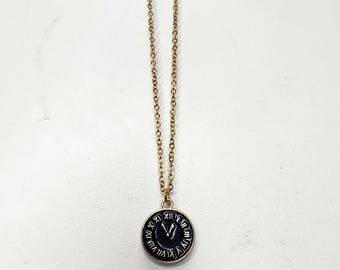 May include: A gold chain necklace with a black clock face pendant. The clock face has Roman numerals and gold hands.