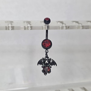 Puede incluir: Anillo de ombligo negro con un dije de murciélago. El anillo presenta una barra negra con una gema roja en la parte superior y una gema roja más grande en el centro. El dije de murciélago tiene detalles de gemas rojas.