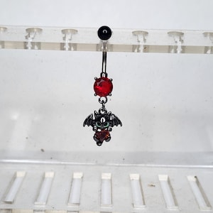 Puede incluir: Un piercing para el ombligo negro con una gema roja y un dije de murciélago. El murciélago tiene alas negras y un cuerpo en forma de corazón rojo. La parte superior del anillo tiene una bola negra.