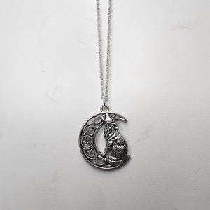 May include: Silver necklace with a pendant featuring a wolf howling at the moon. The moon is crescent shaped and has a pentagram design.