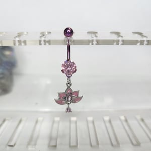 May include: A purple and pink belly button ring. The top ball and the dangling charm are purple. The charm is a pink lotus flower with a pink gem in the center. The belly button ring is displayed on a clear plastic stand.