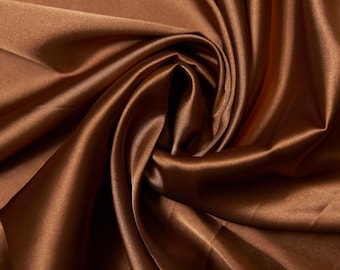 Könnte beinhalten: Nahaufnahme eines luxuriösen, fließenden Stoffes in einem satten, warmen Braunton. Das Material ist glatt und glänzend, mit weichen Falten und subtilen Glanzlichtern, was auf eine Satin- oder Seidenstruktur hindeutet. Der Stoff ist drapiert und gewirbelt, wodurch ein Gefühl von Bewegung entsteht.