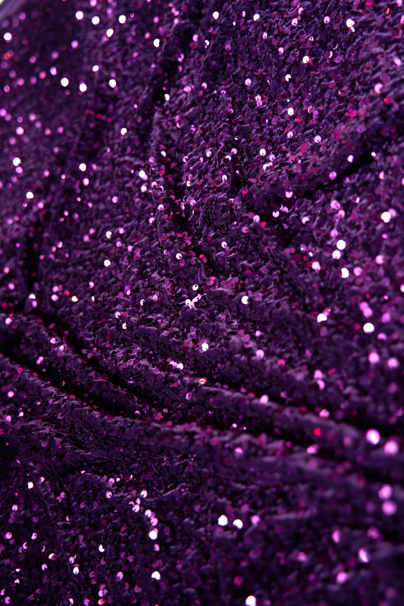 May include: Purple fabric with a sparkly, sequin texture. The sequins are small and densely packed, creating a shimmering effect.