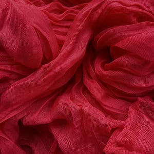 May include: Close-up of a vibrant red fabric with a delicate, sheer texture. The material is gathered and draped, creating soft folds and shadows. The color is a rich, saturated red, with a slightly matte finish. The fabric appears to be lightweight and flowing.