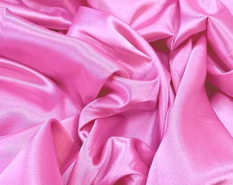 May include: A close-up shot of a vibrant pink satin fabric. The fabric is draped and folded, creating soft shadows and highlights. The smooth, shiny material reflects light, showcasing its luxurious texture. The overall effect is one of elegance and fluidity.