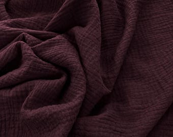 May include: A deep burgundy colored fabric with a distinct crinkled, double gauze texture. The material is draped in soft, flowing folds, highlighting the uneven, puckered surface pattern and the rich, dark red tone of the textile throughout.