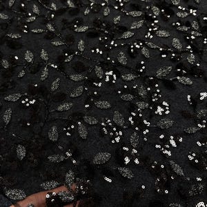 May include: Close-up of black fabric with a leaf pattern. The fabric is embellished with silver sequins and embroidered leaf designs. The texture appears soft and delicate, suitable for evening wear or special occasion garments.