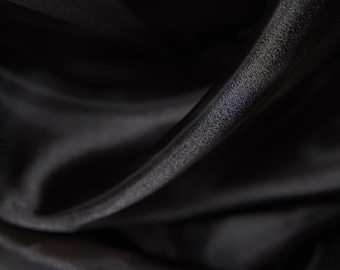 May include: Black sheer fabric with a smooth, silky texture. The fabric is draped and folded, creating soft, flowing lines.