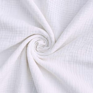 May include: A close-up shot of a white, textured fabric, possibly muslin or gauze, arranged in a spiral pattern. The fabric has a crinkled appearance, with visible woven lines and a soft, flowing drape. The overall impression is of a lightweight, breathable material.