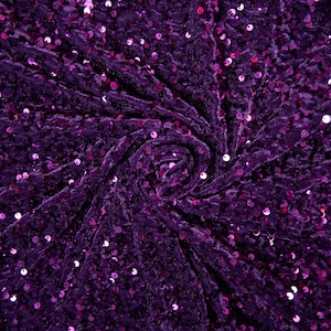 May include: Purple crushed velvet fabric with small, round sequins. The fabric is gathered in the center, creating a swirling pattern.