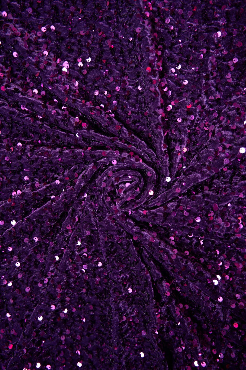 May include: Purple crushed velvet fabric with small, round sequins. The fabric is gathered in the center, creating a swirling pattern.
