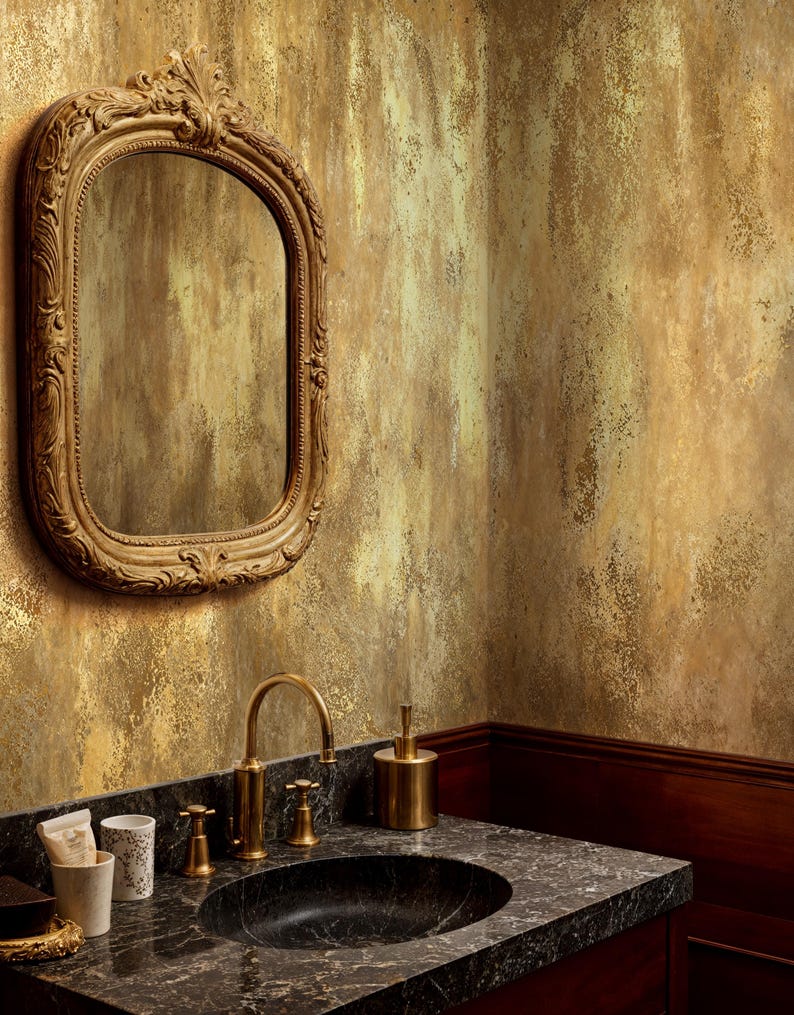 Elegant bathroom vanity featuring a black marble sink and ornate gold mirror. Faux Gold Wall Covering mimicking antique plaster and a wabi sabi metallic effect for a luxury powder room.