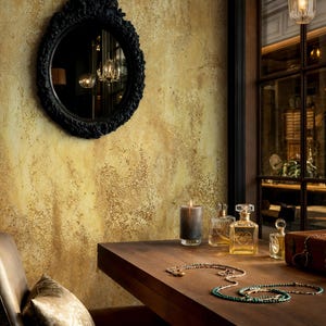 Moody vintage interior styling with an ornate black mirror and glass perfume bottles. Vintage Art Deco Wallpaper showing a printed grunge gold texture for a dramatic home office or vanity.