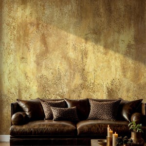 Masculine living room styling with a brown leather chesterfield sofa and leopard print pillows. Faux Gold Texture Peel and Stick Wallpaper displaying a printed grunge plaster effect without real metallic shine.