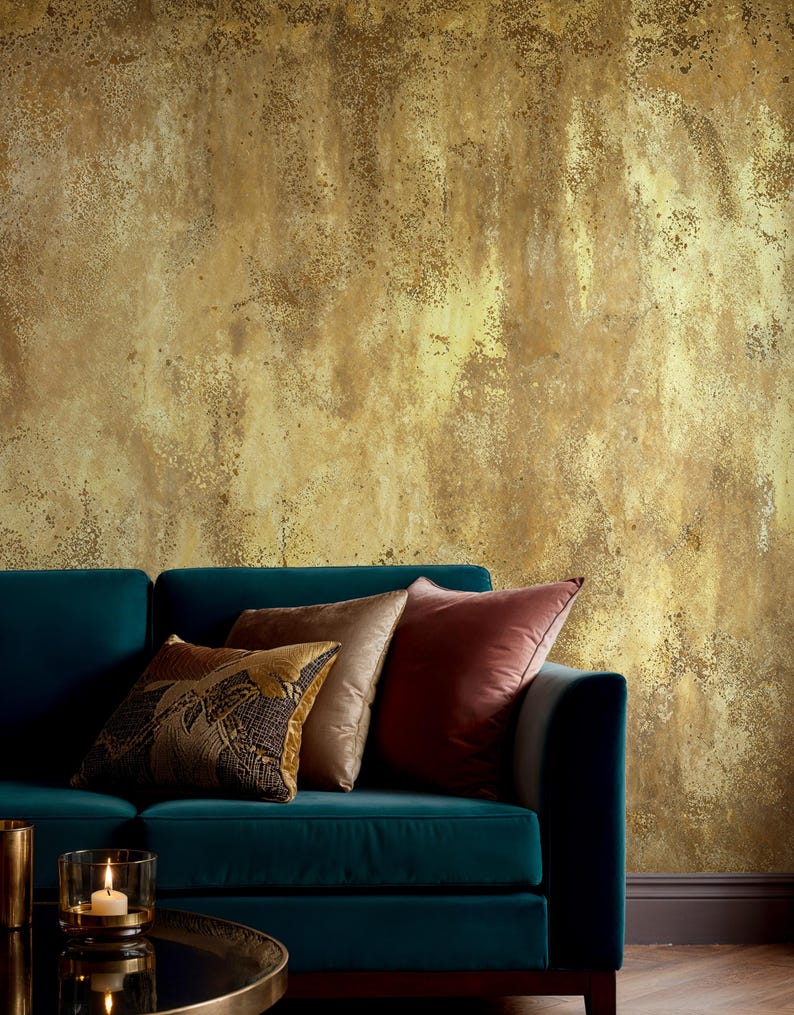 Modern living room interior with a teal velvet sofa and elegant pillows. Faux Gold Texture Wallpaper featuring a distressed metallic effect and rustic grunge finish for a sophisticated wabi sabi decor.