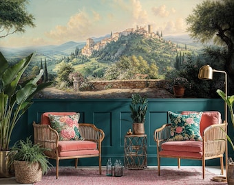 Op de afbeelding: Een woonkamer met twee koraalkleurige fauteuils met bloemenkussens, geplaatst tegen een muurschildering van een Italiaans landschap. De kamer is ingericht met potplanten, een gouden lamp en een geweven bijzettafel, wat een gezellige sfeer creëert.