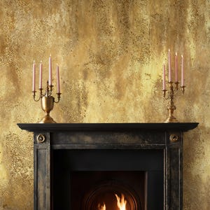 Classic black fireplace mantel styled with vintage brass candlesticks. Art Deco Plaster Wall Covering acting as a distressed gold backdrop, creating a warm and inviting rustic glam atmosphere.