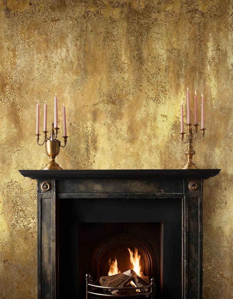 Classic black fireplace mantel styled with vintage brass candlesticks. Art Deco Plaster Wall Covering acting as a distressed gold backdrop, creating a warm and inviting rustic glam atmosphere.