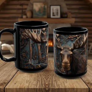 Peut inclure: Deux mugs à café noirs avec un motif de wapiti détaillé. L'un des mugs présente un motif de bois de wapiti avec le nom "MARK". L'autre mug présente un gros plan du visage d'un wapiti. Les mugs sont posés sur une surface en bois.