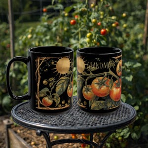 Peut inclure: Deux mugs en céramique noirs avec un motif de plant de tomates. L'un des mugs présente un soleil et l'autre le mot "GRANDMA" en blanc. Les mugs sont sur une table en métal noir avec un arrière-plan de jardin.