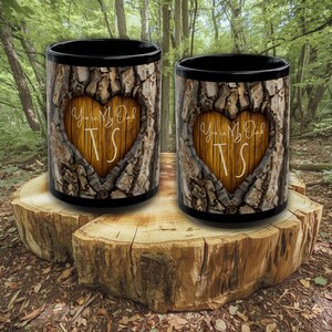 Peut inclure: Deux tasses à café noires avec une texture d'écorce et une découpe en forme de cœur. Le cœur révèle un motif de grain de bois avec les mots "You're My Oak" et les initiales "TS" en écriture cursive. Les tasses sont présentées sur une souche d'arbre.