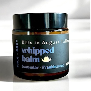 May include: A small, round jar of whipped balm with a black lid and a dark label. The label features the text "Ellis in August Tallow" and "whipped balm" in blue, with "Lavender + Frankincense" below. A small cowboy hat graphic is also present.